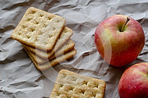 Ripe Red Apples and square crackers lying on crumpled wrapping paper