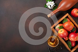 Ripe red apples in wooden box with branch of white flowers, glass and bottle of cider on a rusty background