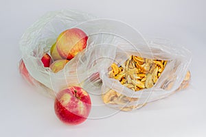 Ripe red apples and yellow dried slices of apples in transparent plastic crumpled cellophane bags on white background. Top view