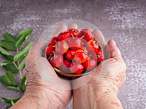 Ripe red cherries in a ceramic bowl on the palm of senior woman