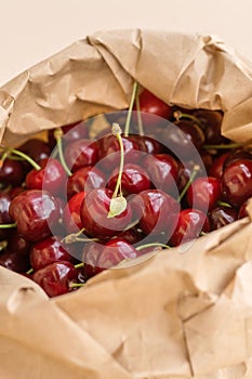 Ripe red cherries in an eco-friendly paper bag on a beige background. Close-up