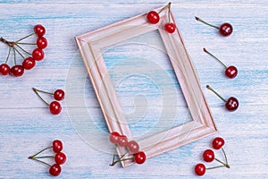 ripe red cherries and a photo frame on a blue wooden table. top view