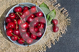 ripe red cherry berries in a round blue bowl on a dark background and mat