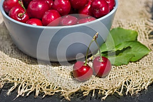 ripe red cherry berries in a round blue bowl on a dark background and mat