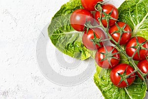 Ripe red cherry tomatoes on green salad leaves, stone table, top view with copy space