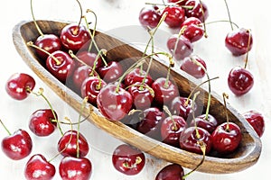 Ripe red cherry with water drops in a wooden elongated plate on an old painted table close up