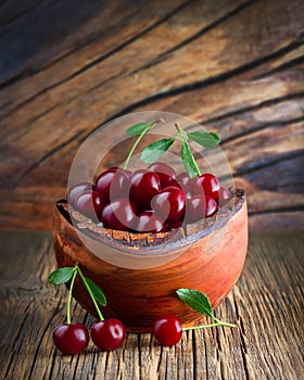 A ripe red cherry in a wooden bowl on the table. Green leaves. Photo