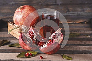 Ripe red open pomegranate , a whole pomegranate in a box , a glass of juice on a dark wooden