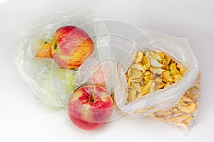 Ripe red orange seasonal apples and yellow dried slices of apples in transparent plastic cellophane bags on white background Fruit