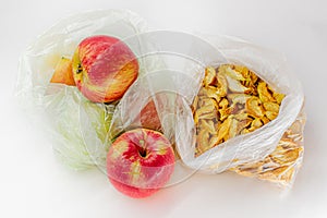 Ripe red orange seasonal apples and yellow dried slices of apples in transparent plastic crumpled cellophane bags on white backdro