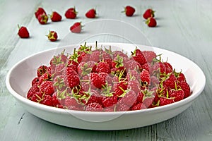 Ripe red raspberries with stalks are poured into a white ceramic plate