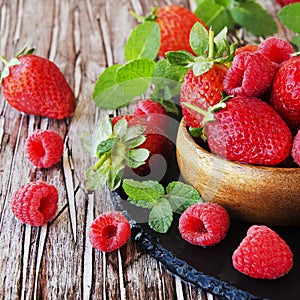 ripe red raspberries and strawberries in wooden bowl, selective focus