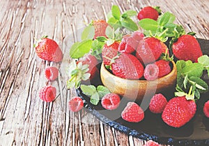 Ripe red raspberries and strawberries in wooden bowl, selective focus