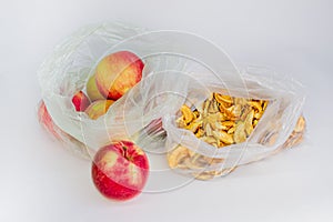 Ripe red seasonal apples and yellow dried slices of apples in transparent plastic crumpled cellophane bags on white backdrop. Frui
