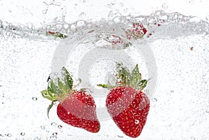 Ripe red strawberries are thrown and dropped into sparkling water, many bubbles