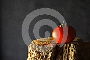 RIPE RED TOMATO ON A PIECE OF RAW WOOD AGAINST A GREY BACKGROUND