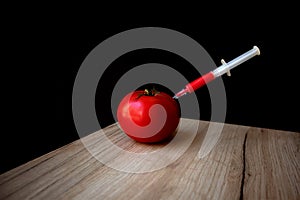 Ripe red tomato on a wooden board with syringe inside