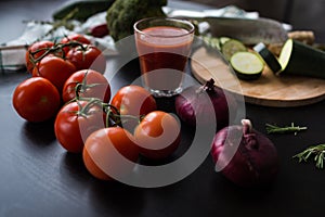 Ripe red tomatoes and big red onions are lying on a black stylish table. in the background we see a glass of tomato