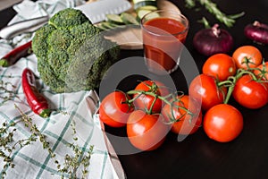 Ripe red tomatoes are lying on a black stylish table. in the background we see a glass of tomato juice, red onions