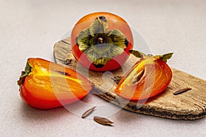 Ripe single persimmon. Fresh whole fruit, half sliced, seeds. Wooden cutting board, stone concrete background