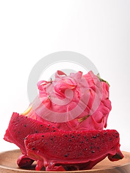 Ripe sliced and complete pink pitaya also called  dragon fruit on wooden plate isolated on white background.