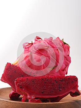 Ripe sliced and complete pink pitaya also called  dragon fruit on wooden plate isolated on white background.