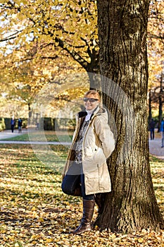 Ripe, smiling woman in autumn park at tree