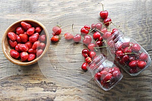 Ripe strawberries and cherries , glass jars. Wood background, rustic style.