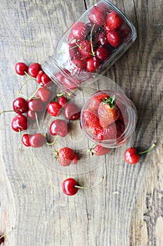 Ripe strawberries and cherries , glass jars. Wood background, rustic style.