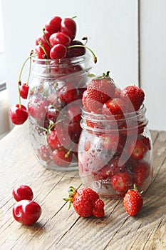 Ripe strawberries and cherries , glass jars. Wood background, rustic style.