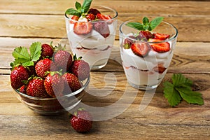 Ripe strawberries and layered cream cheese dessert on wooden background