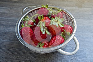 Ripe strawberries in a small stainless steel colander on kitchen counter