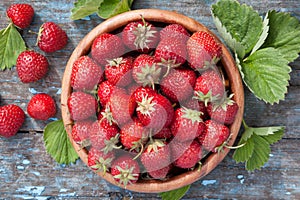 Ripe strawberries in wooden bowl and green leaves