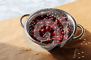 Ripe sweet cherries in metal colander with water drops. Washed garden juicy berries on kitchen table. Still life from everyday