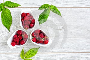 Ripe sweet and fresh raspberries in a white ceramic bowl with leaves