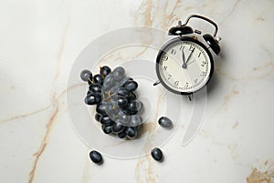 Ripe sweet grapes and alarm clock on light table