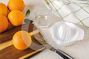 Ripe sweet oranges, plastic manual citrus juicer, fruit knife and empty glass on the kitchen table. Making freshly squeezed juice