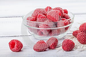 Ripe sweet raspberries in bowl on white wooden table