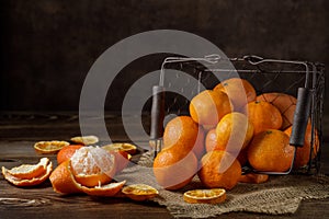 Ripe tangerines and clementines spilled out of an old metal basket on a rustic wooden table .Dark background, with a copy of the s
