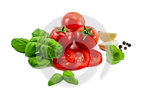 Ripe tomato cut into slices along with basil and garlic on a white background