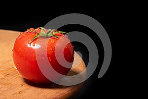 Ripe tomato on a wooden board isolated against black background.