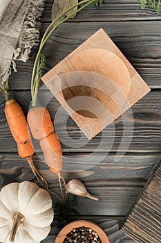 Ripe unpeeled carrot with green haulm. Empty bowl on kitchen wooden table. Flat lay view. Vegetables and flavorings.