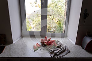 Ripe watermelon cut into slices on a light table by window, still life, top view