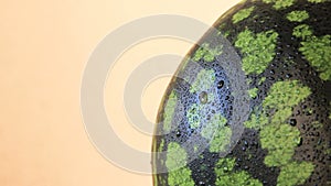 Ripe watermelon rind with waterdrops rotating slowly, close up shoot, warm background