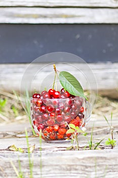 Ripe wet cherries and strawberries in a transparent cup on wood boards. Fresh red cherry fruits in summer garden