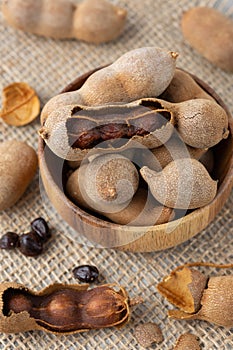 Ripe whole and shelled tamarind fruits with seeds in wooden bowl closeup on jute background