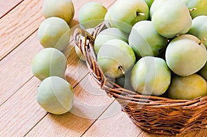 Ripe yellow-green plums in a wicker basket on a wooden table