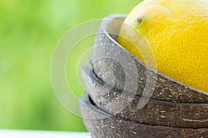 Ripe yellow lemon in coconut shell bowl on green foliage background. Organic cosmetics healthy lifestyle detox wellness