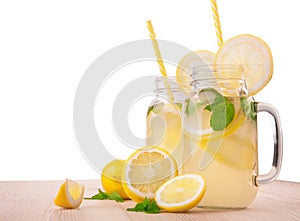 Ripe yellow lemons, fresh mint and mineral water in two transparent jugs on a light wooden table, isolated on a white background.