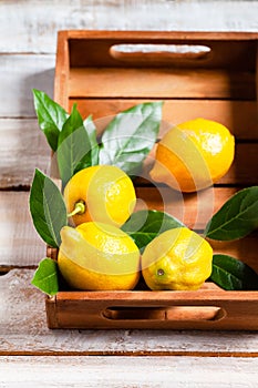 Ripe yellow lemons with leaves in wooden box. Ingredients for refreshing summer beverage - homemade lemonade. Close up, macro view